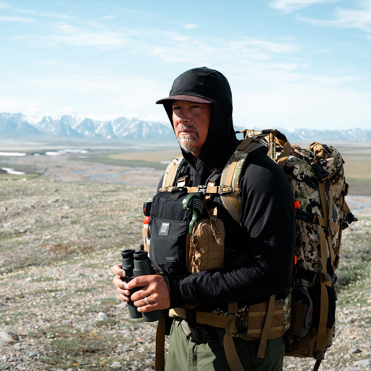 Casey Anderson in the mountains with his pack and binoculars