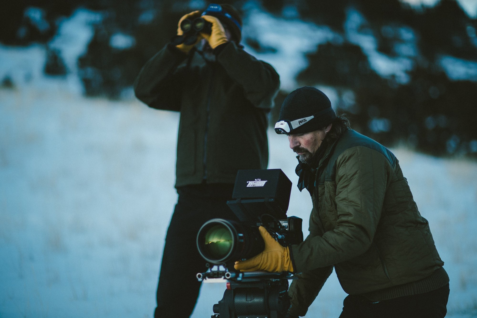A camera crew working in the snow with a cinema camera and binoculars